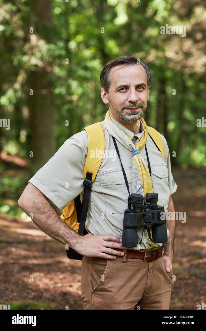 Portrait vertical de l'homme adulte en tant que chef de scout regardant la caméra à l'extérieur dans la forêt et portant l'équipement de randonnée Banque D'Images