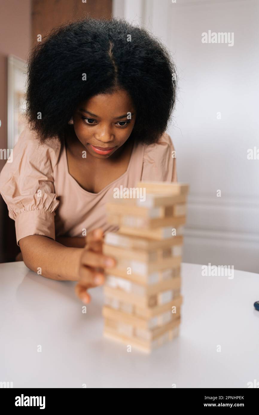 Gros plan portrait vertical d'une femme afro-américaine sérieuse jouant un bloc de tour avec des amis divers, en sortant un bloc de tour bancale. Banque D'Images