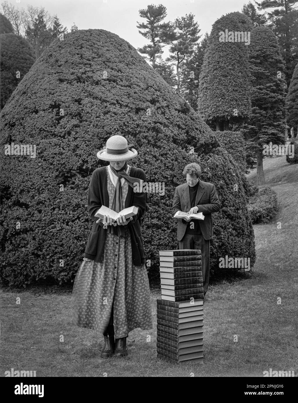 Homme et femme lisant en se tenant près d'une pile de livres dans le jardin topiaire Banque D'Images