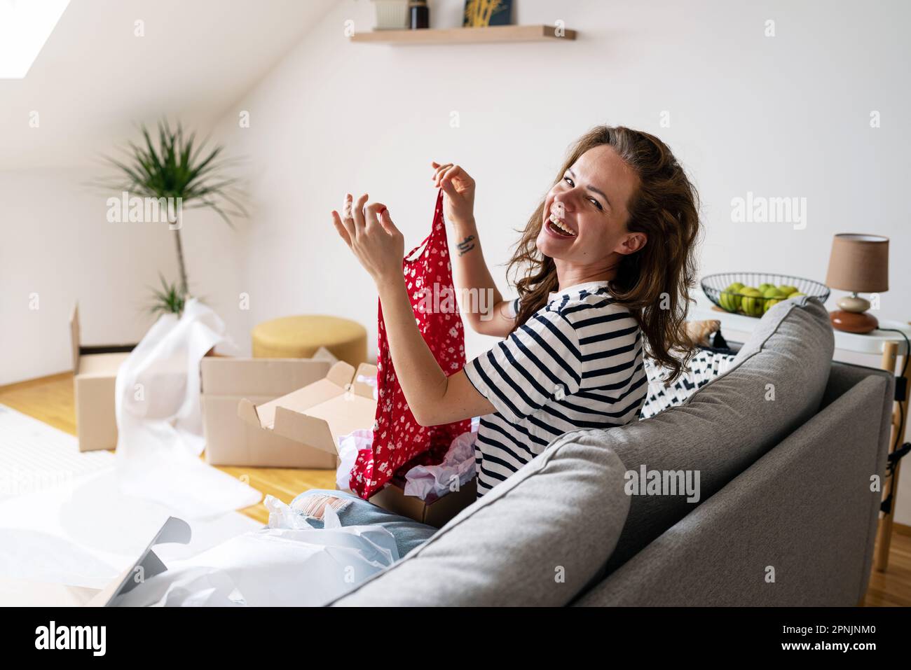 Bonne femme déballant ses robes et en riant. déménagement dans une nouvelle maison et déballage des vêtements. Banque D'Images