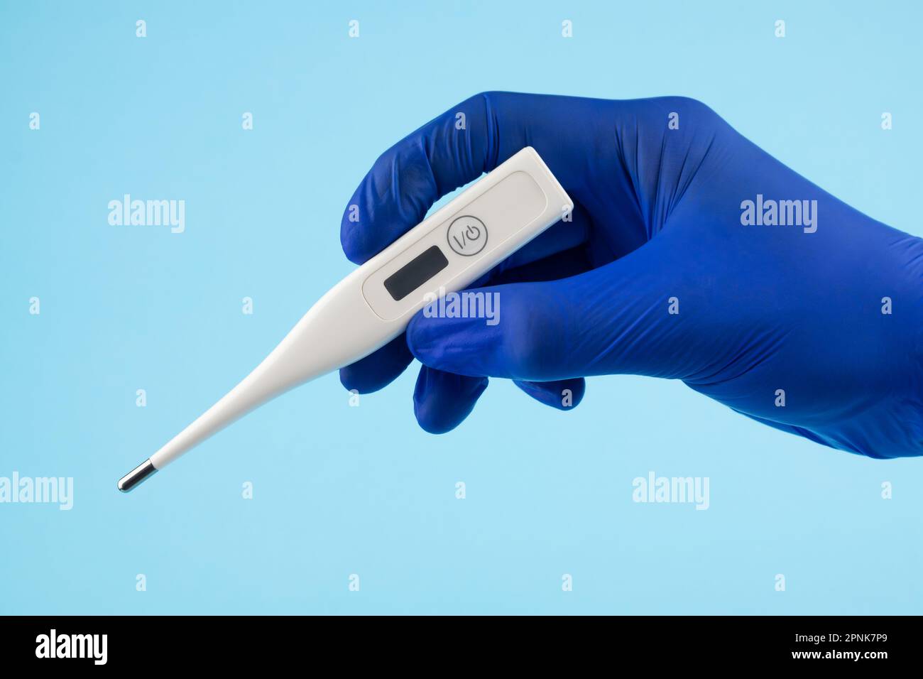 La main d'un homme en gants bleus tient un thermomètre sur fond bleu. Un médecin portant des gants en latex bleu montre un thermomètre électronique. Banque D'Images
