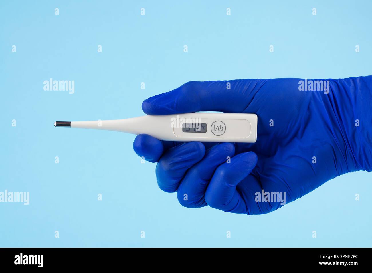 La main d'un homme en gants bleus tient un thermomètre sur fond bleu. Un médecin portant des gants en latex bleu montre un thermomètre électronique. Banque D'Images
