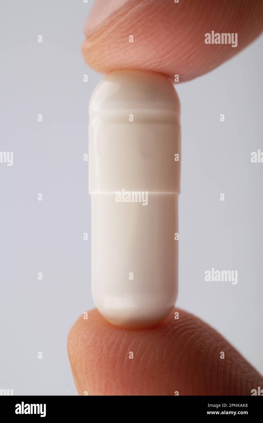 Les doigts maintiennent la pilule très près. Vue macro supplémentaire de la pilule blanche. Banque D'Images