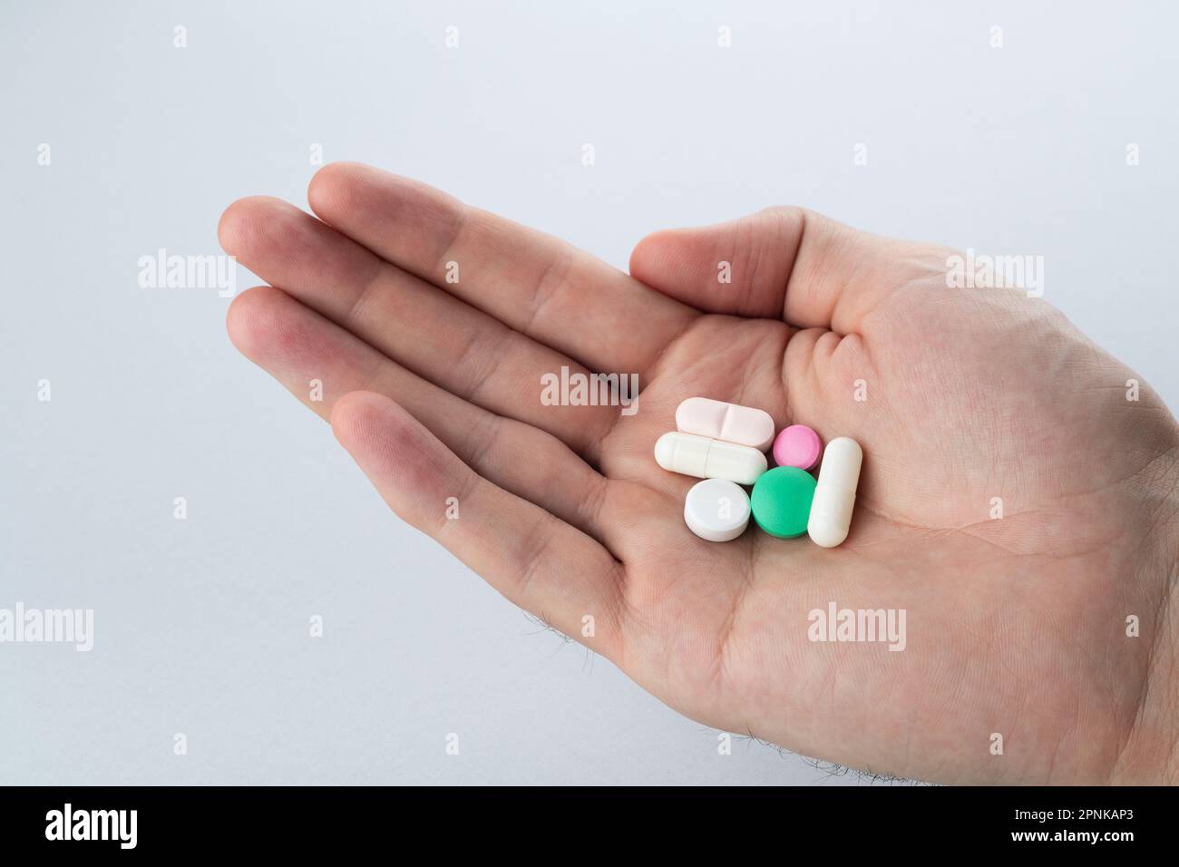 Main mâle tenant des pilules multicolores à la main sur fond gris, prenant votre médicament. Gros plan Banque D'Images