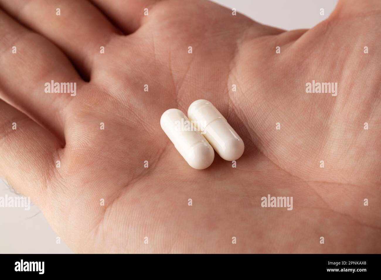 Main mâle tenant deux pilules à la main sur fond gris, prenant votre médicament. Gros plan Banque D'Images