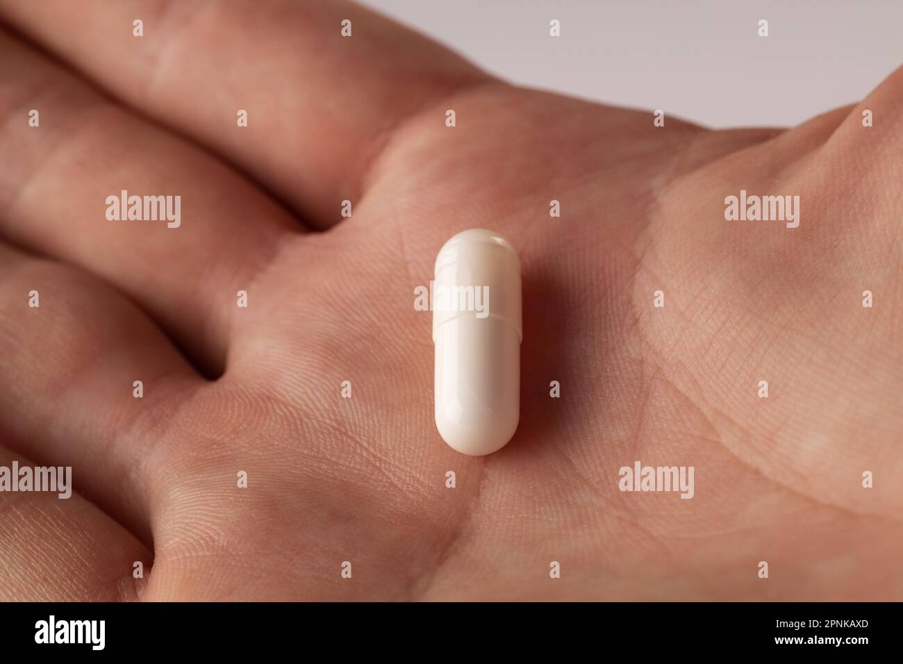 Main masculine tenant une pilule à la main sur fond gris, prenant votre médicament. Gros plan Banque D'Images