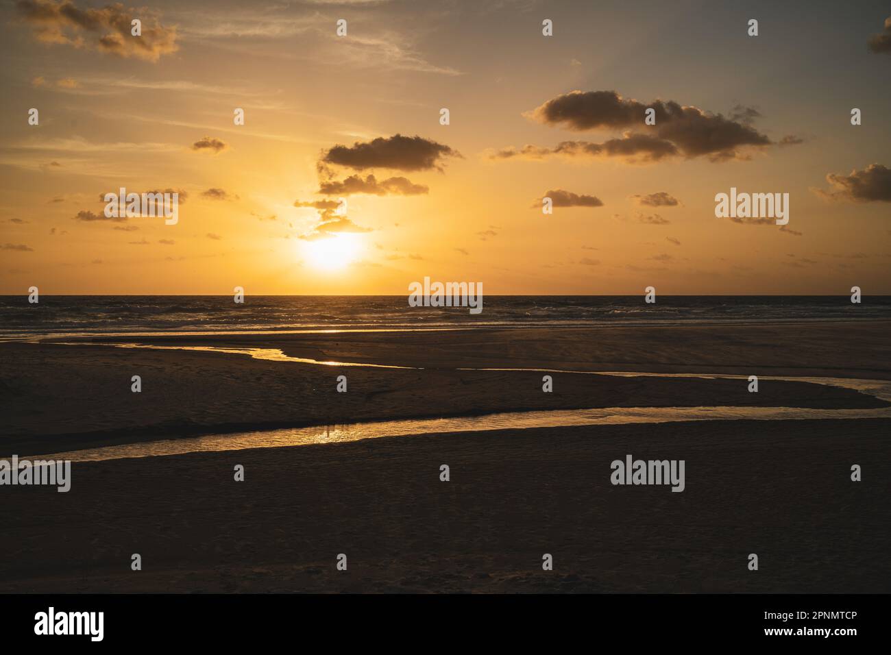 Lever de soleil d'or tôt sur la plage pris de la plage montrant le cours d'eau traversant le sable. Photo prise face à l'océan Pacifique. Banque D'Images