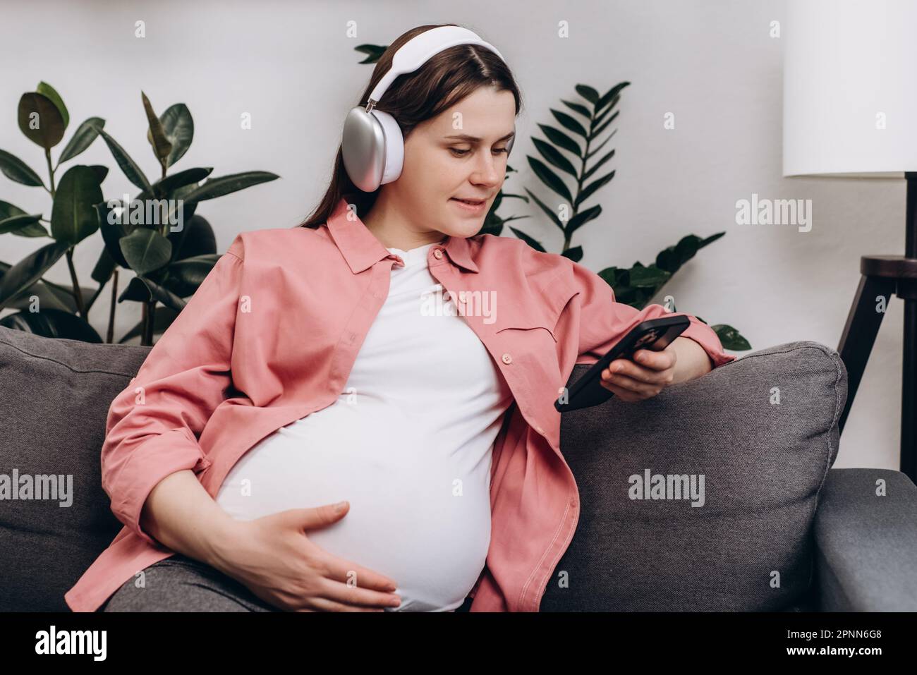 Gros plan d'une belle jeune femme enceinte porter un casque sans fil tenir un smartphone regarder l'écran du téléphone à l'aide de l'application de lecteur mobile écouter MU en ligne Banque D'Images