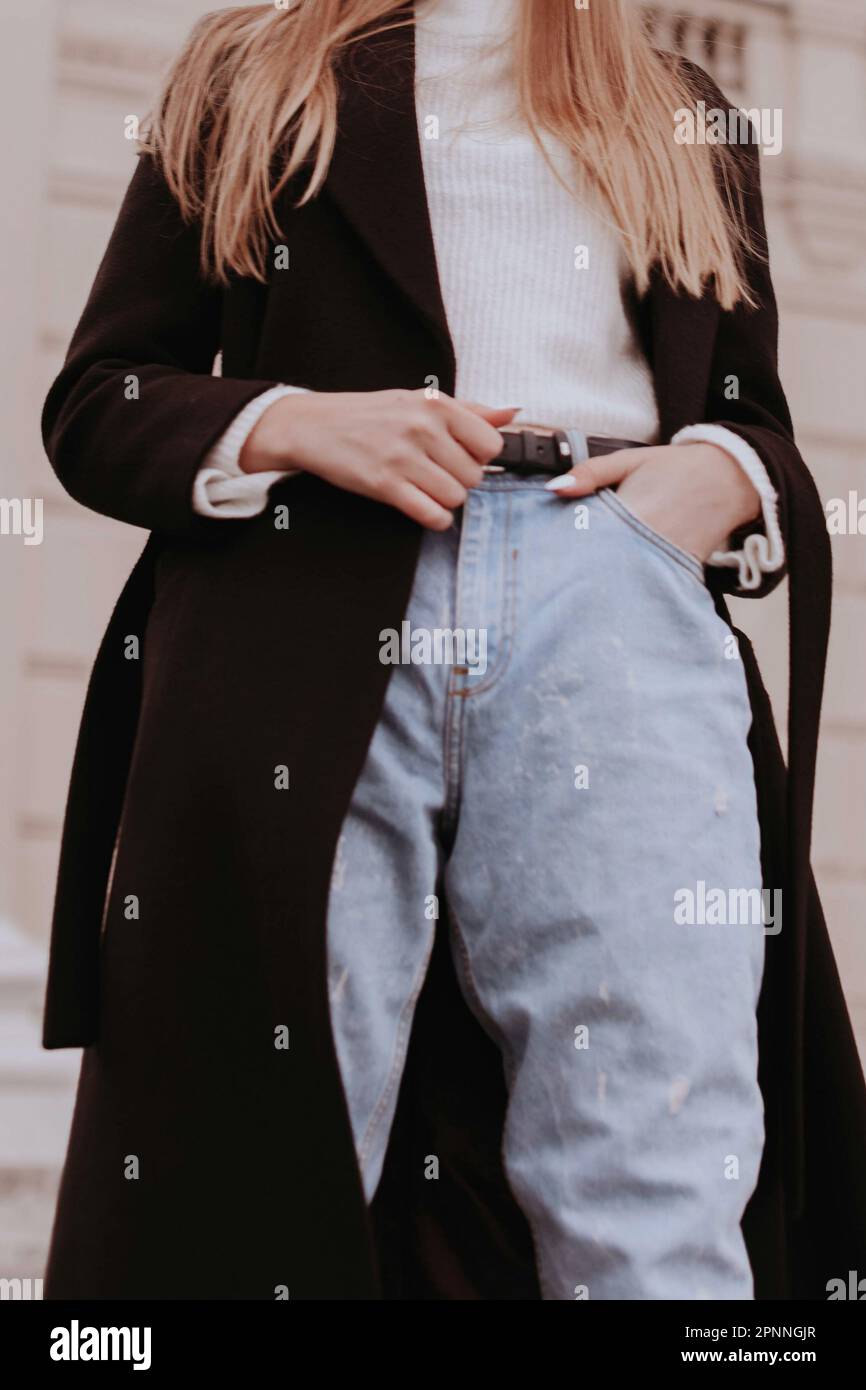 Silhouette féminine en Jean bleu denim, chandail blanc et manteau noir. Portrait en extérieur à la lumière du jour. Automne hiver style rue concept de tissu Banque D'Images