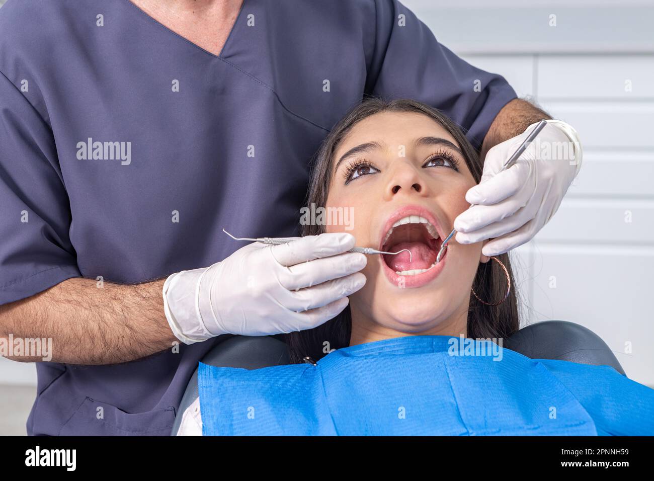 Croiser le dentiste masculin en utilisant le miroir et la sonde pour vérifier les dents du patient adolescent pendant le travail dans le bureau de la clinique moderne Banque D'Images