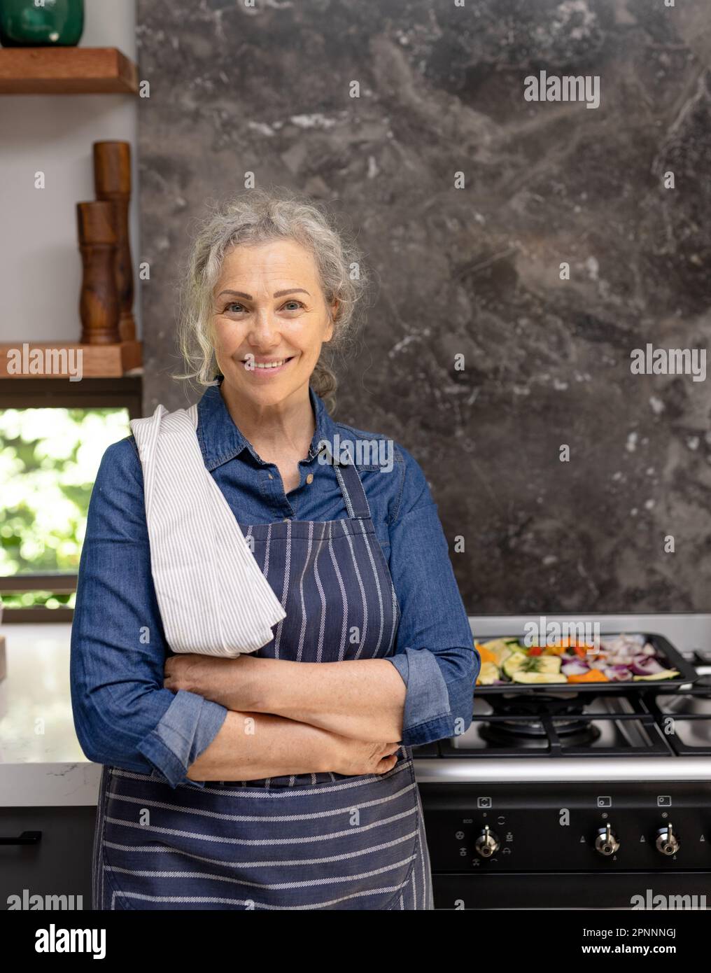 Portrait d'une femme caucasienne âgée heureuse portant un tablier et souriant dans la cuisine Banque D'Images