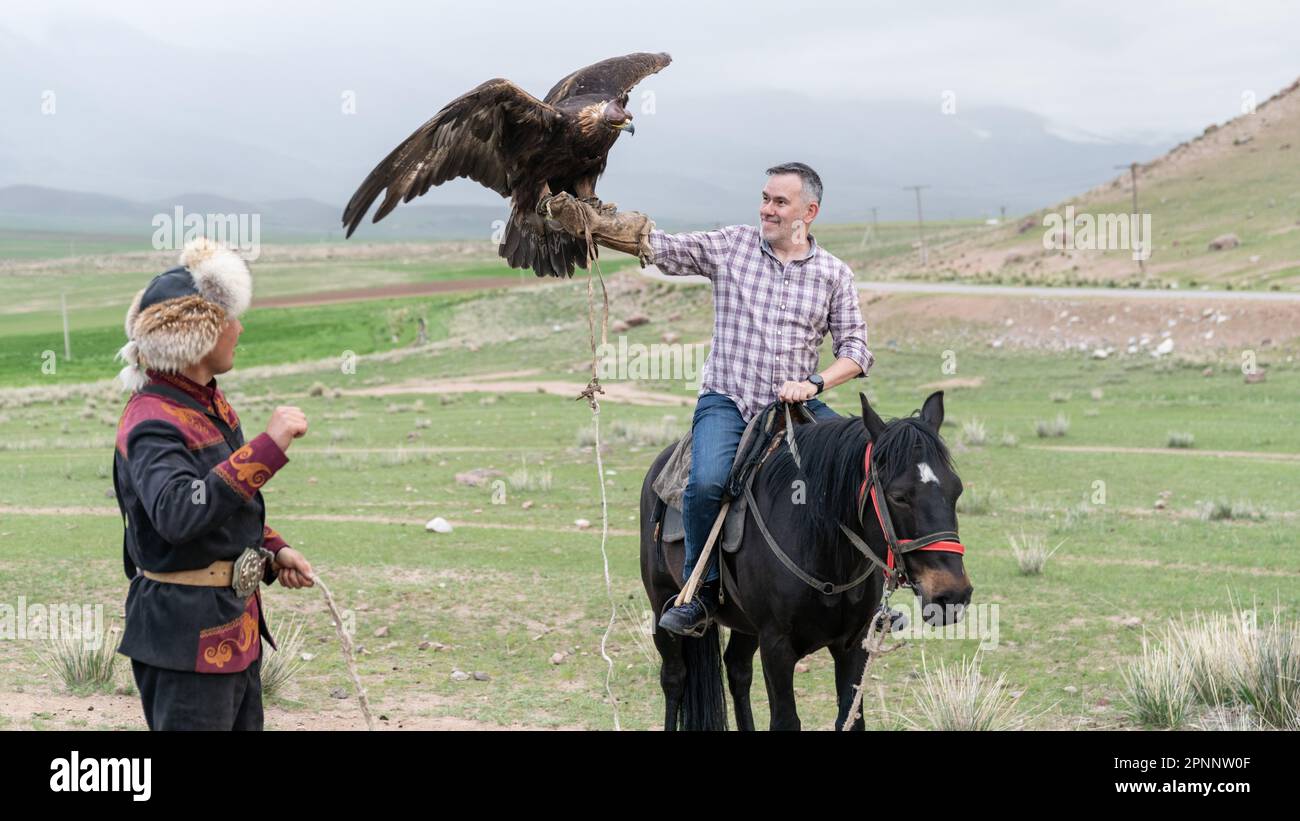 Issyk Kul, Kirghizistan - Mai 2022: L'entraîneur d'aigle aidant un touriste à tenir son aigle d'or. Le tourisme traditionnel au Kirghizistan Banque D'Images