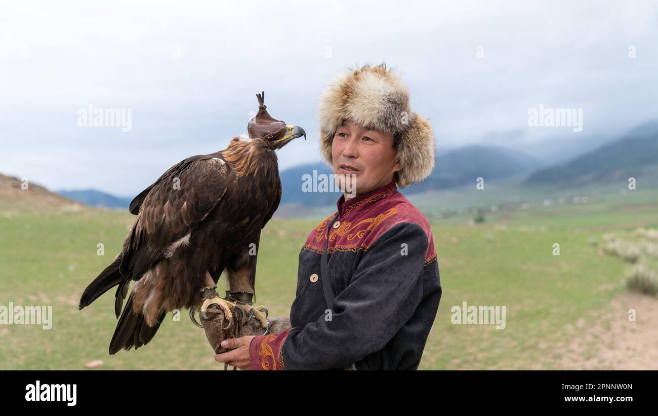 Issyk Kul, Kirghizistan - Mai 2022: L'entraîneur d'aigle et son aigle doré, qualifié dans l'entraînement des aigles pour la chasse, en utilisant les techniques traditionnelles sont passées Banque D'Images