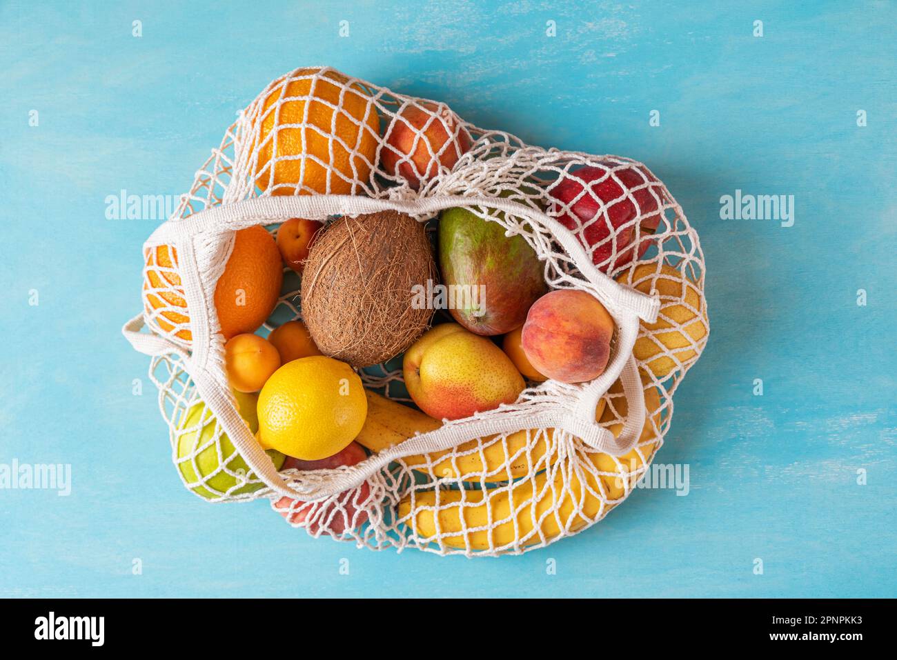 Vue de dessus du sac à provisions en maille avec des fruits tropicaux écologiques bio sur fond bleu. Respect de l'environnement et concept sans plastique Banque D'Images