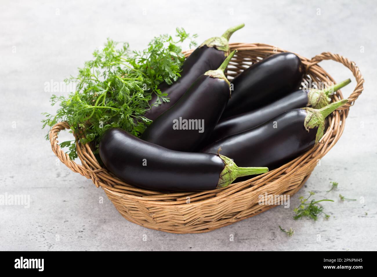 Panier en osier avec aubergines mûres et herbes sur fond gris texturé Banque D'Images