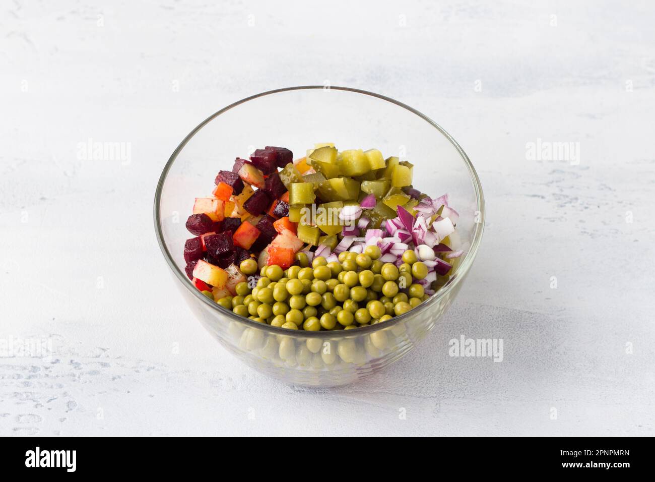 Bol en verre avec salade vinaigrette de légumes, betteraves, carottes, pommes de terre, pois verts en conserve et oignons rouges sur fond bleu clair. Cuisine homema Banque D'Images