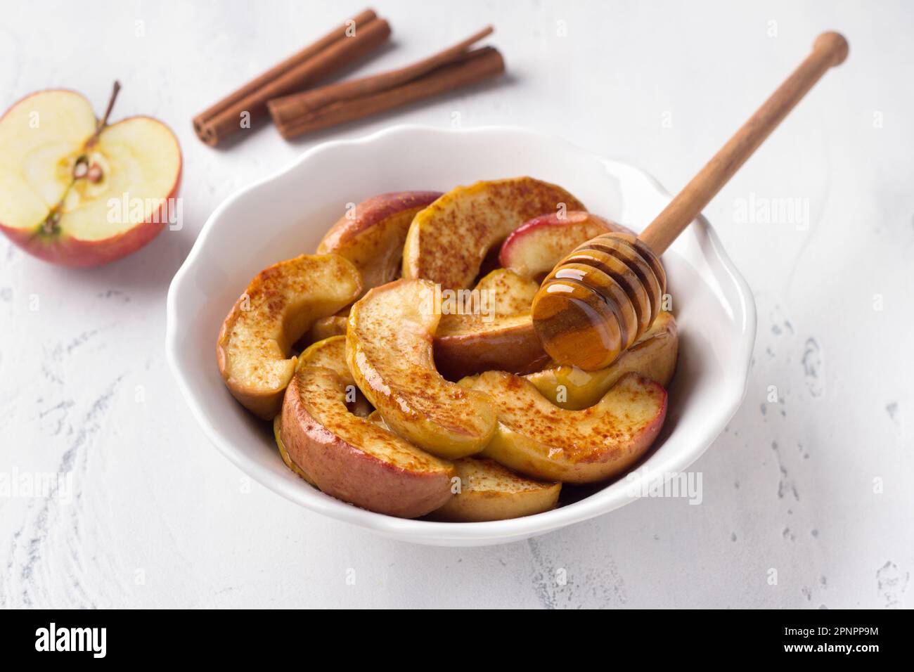 Un bol blanc de tranches de pomme cuites à la cannelle sur fond bleu clair. Délicieux dessert vegan maison Banque D'Images