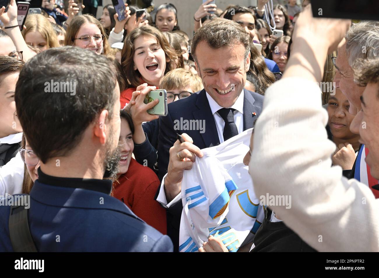 Ganges, France. 20th avril 2023. Le président français Emmanuel Macron  signe un maillot de club de football de l'Olympique de Marseille lors d'une  visite à l'école intermédiaire de Ganges, dans le sud