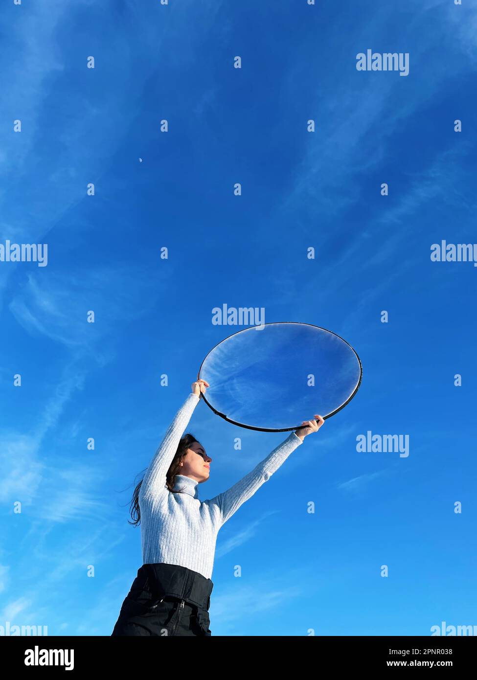 Femme tenant un réflecteur photographique rond dans ses mains contre le ciel bleu Banque D'Images