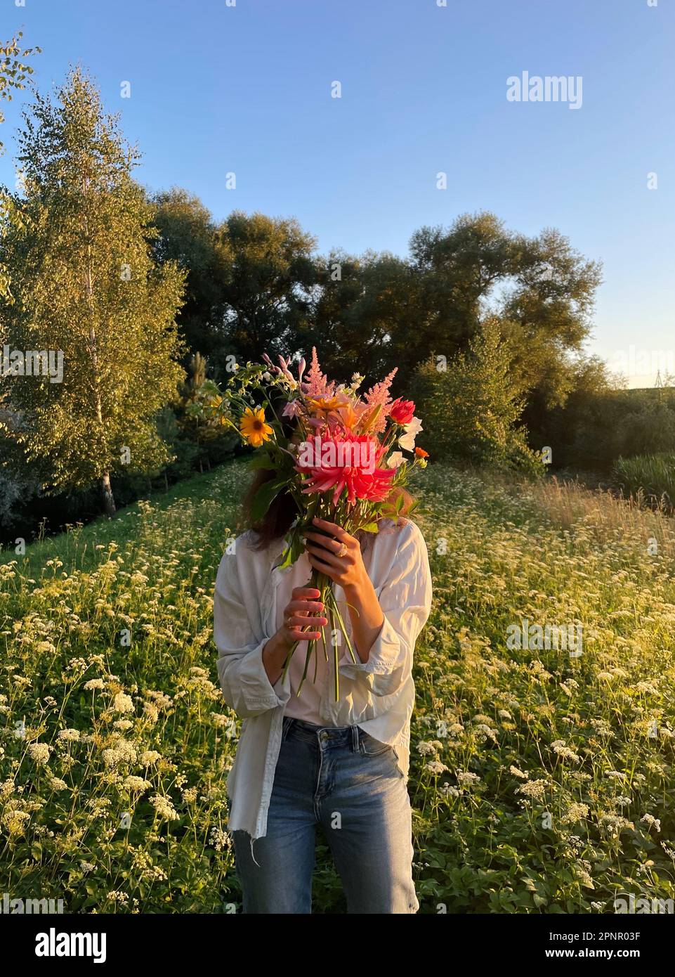 Femme debout dans un pré d'été tenant un bouquet de fleurs devant son visage Banque D'Images