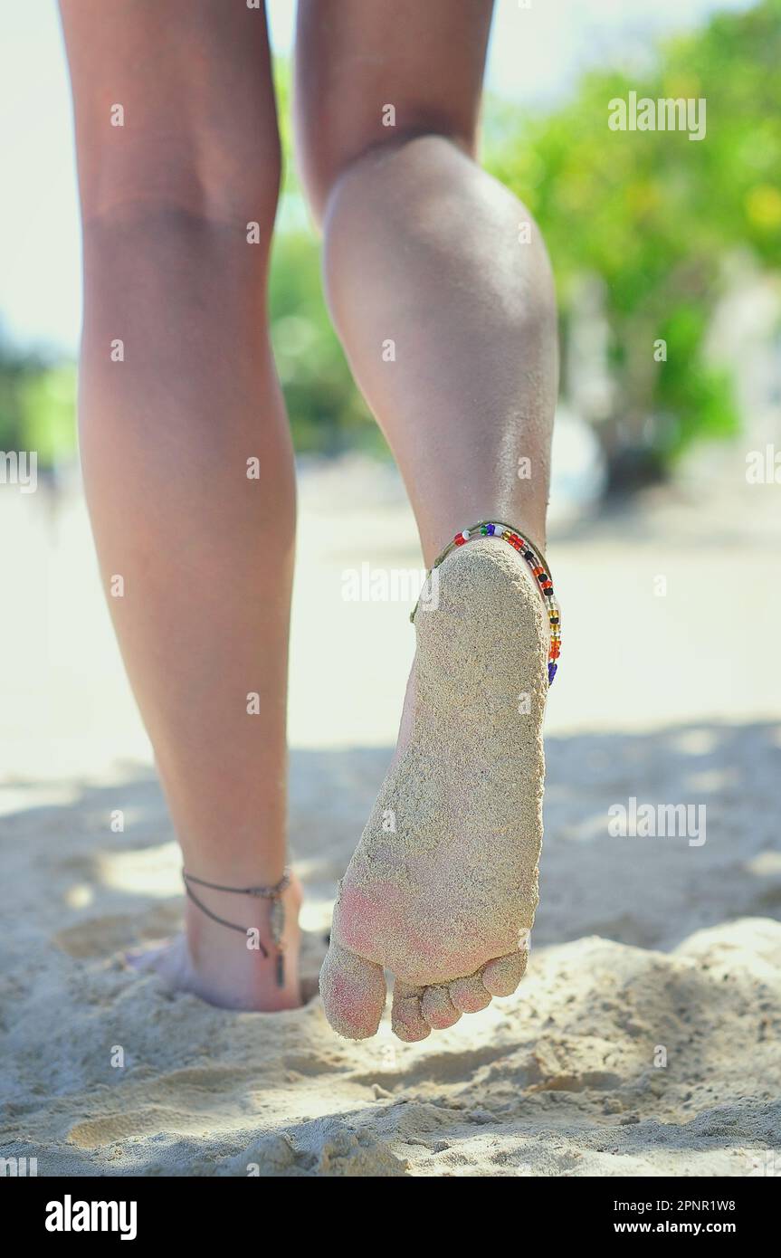Vue arrière d'une jeune femme, portant des bracelets de cheville de perles marchant pieds nus sur la plage, Jamaïque Banque D'Images