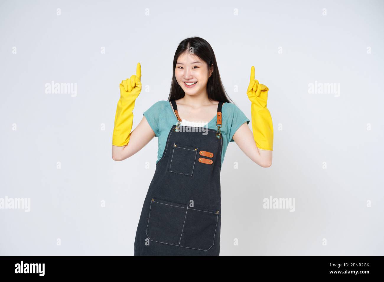 Portrait d'une jeune femme portant des gants en caoutchouc jaune pour la protection des mains et pointant vers un espace de copie vide isolé sur fond blanc. Banque D'Images