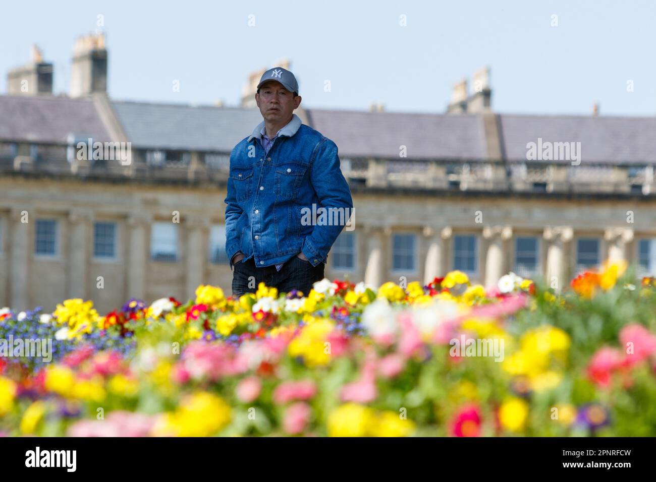 Bath, Royaume-Uni. 20th avril 2023. Avec le célèbre Royal Crescent de Bath à l'arrière-plan, un homme est photographié en marchant le long des lits de fleurs colouful dans le Royal Victoria Park. Les prévisionnistes prédisent que le temps sera plus frais et plus couvert dans les prochains jours. Credit: Lynchpics/Alamy Live News Banque D'Images