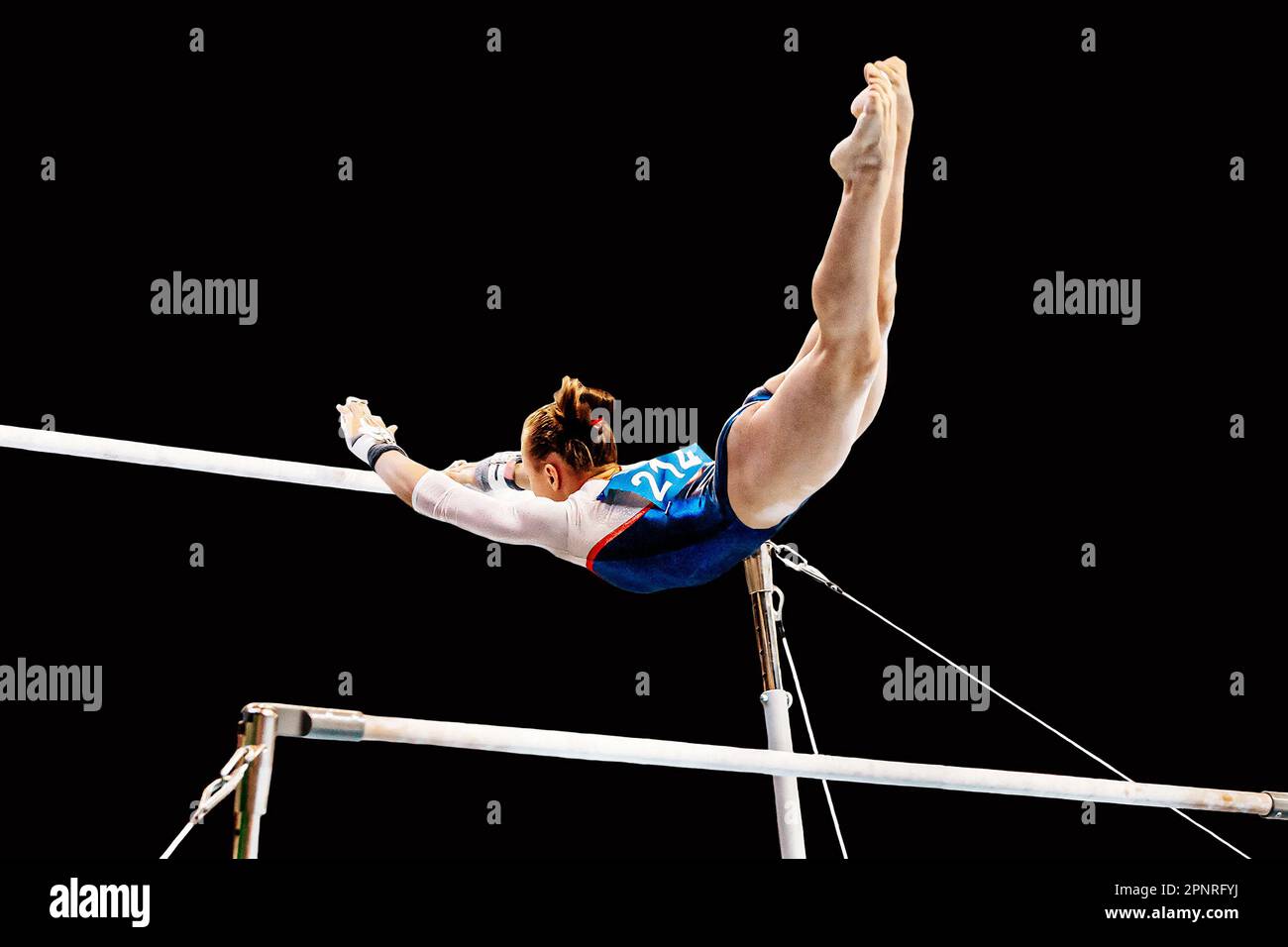 exercice de gymnaste féminin sur des barres inégales en gymnastique artistique, élément de vol de la barre basse à la barre haute, fond noir Banque D'Images