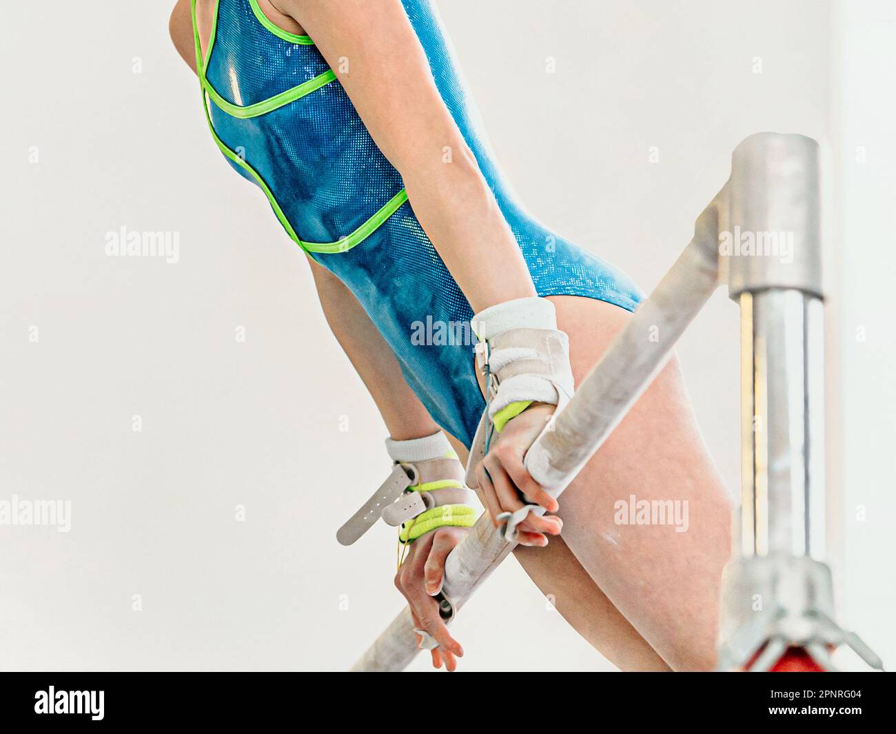 gros plan de la gymnaste de fille sur des barres inégales en gymnastique artistique, fond clair, maillot de bain bleu et poignées de mains Banque D'Images