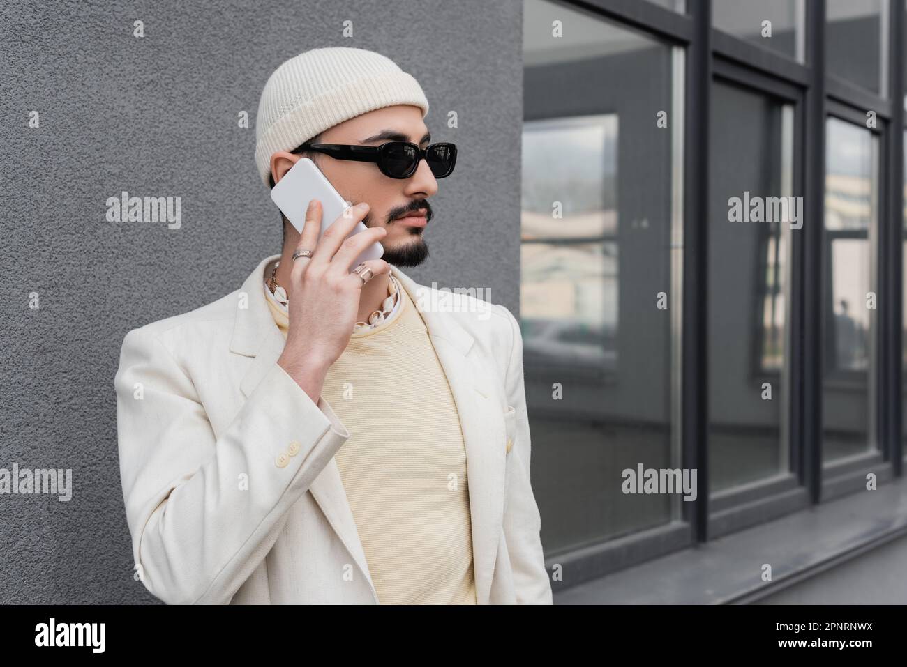 Homme homosexuel branché dans des lunettes de soleil parlant sur téléphone mobile sur la rue urbaine, image de stock Banque D'Images
