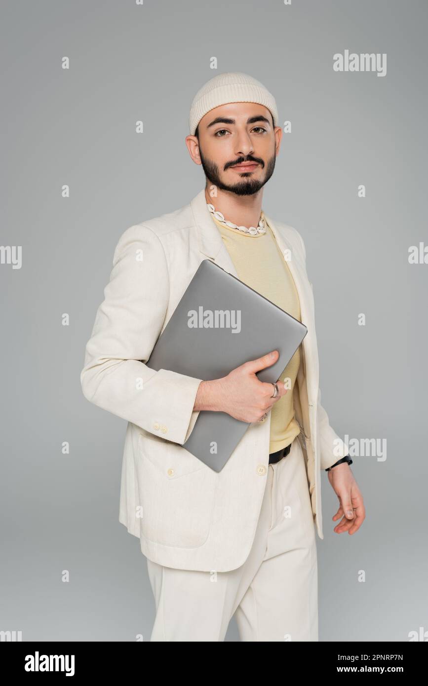 Homme homosexuel bien habillé en costume tenant l'ordinateur portable isolé sur gris, image de stock Banque D'Images
