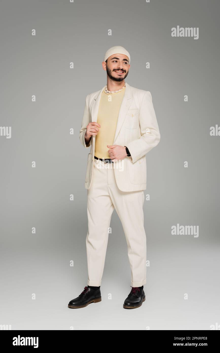 Gai homosexuel homme en costume beige et chapeau touchant la veste sur fond gris, image de stock Banque D'Images