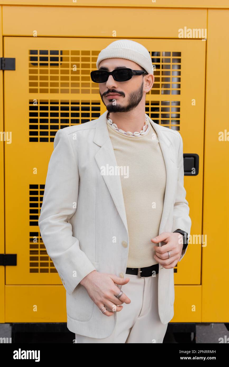 Homme homosexuel à la mode en chapeau et lunettes de soleil debout sur la rue urbaine, image de stock Banque D'Images