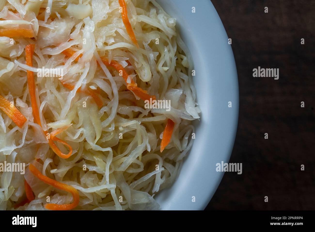 Choucroute maison dans un bol en céramique sur fond de bois, gros plan, vue de dessus. Chou finement coupé avec des carottes, fermenté par des bactéries lactiques avec Banque D'Images
