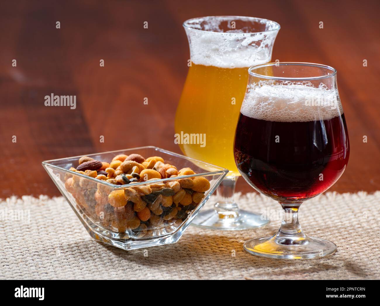 Verres de bière blonde jaune belge et marron foncé faits à l'abbaye servis au bar avec noix de fête, gros plan Banque D'Images