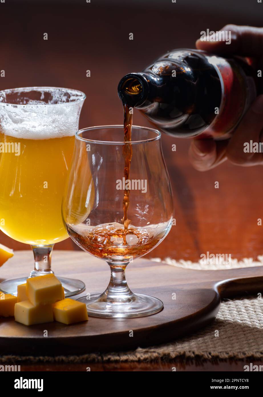 Verres de bière blonde jaune belge et brune foncée fabriqués en abbaye et en bois avec une variété de fromages belges, plats et bières assortis en Belgique Banque D'Images