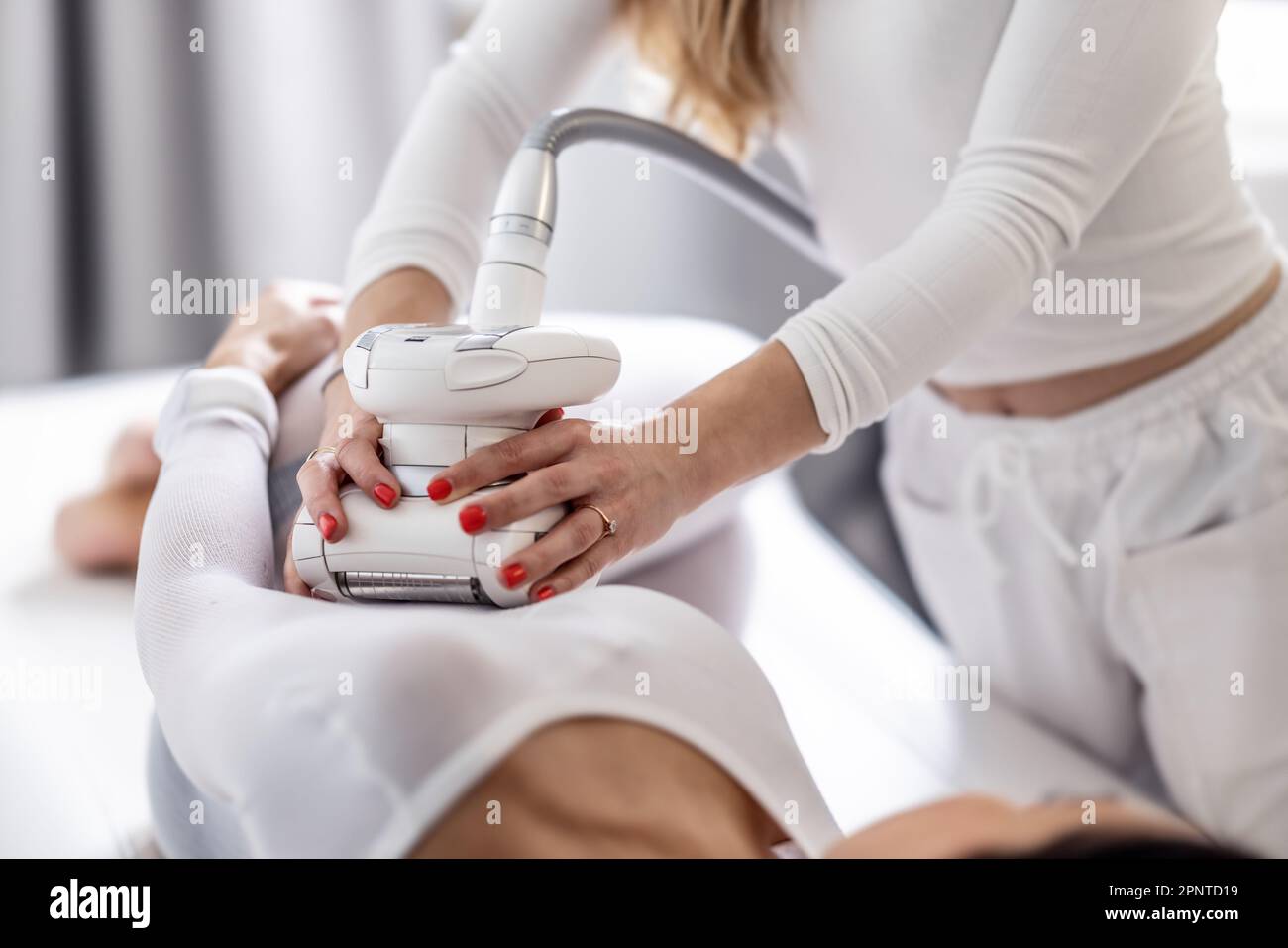 Une esthéticienne tient un dispositif d'endermologie GPL avec les deux mains scannant le corps féminin de son client. Banque D'Images