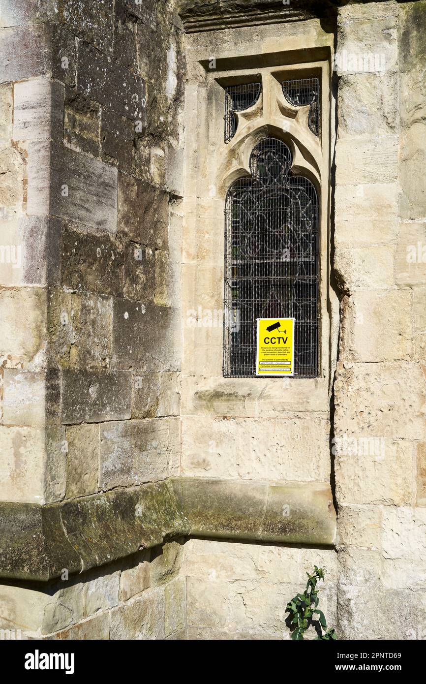 Avis jaune de CCTV affiché dans la fenêtre au plomb d'une ancienne église en pierre protégée par un grill en métal Banque D'Images