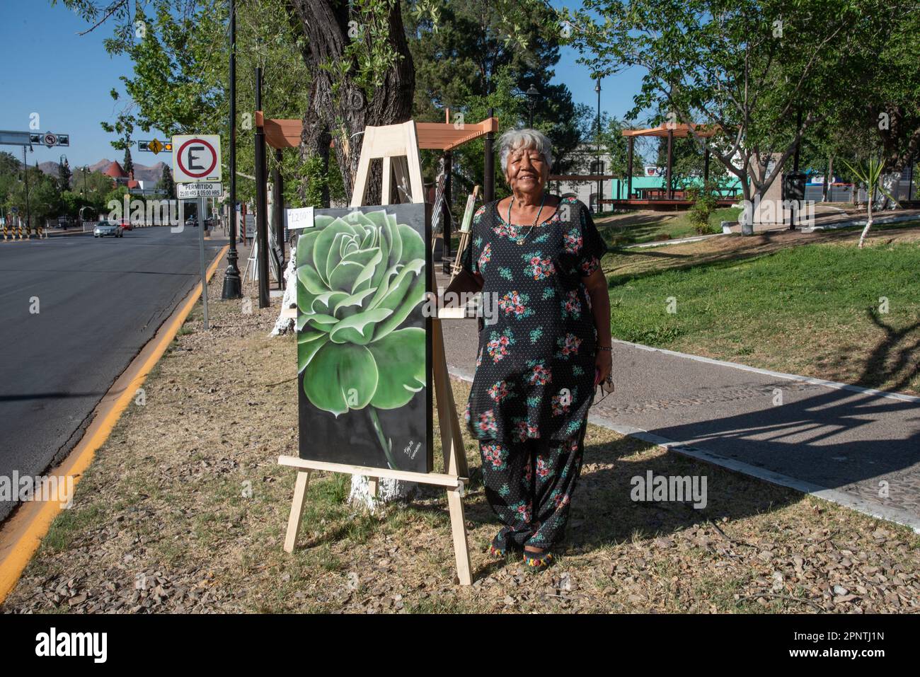 Esther Villalpando se tient avec une de ses peintures au Parque Lerdo à Chihuahua, Mexique sur 24 avril 2022. Après une hiatus de deux ans, les artistes peuvent maintenant exposer et vendre leurs œuvres au parc. Villalpando dit, "l'art et la culture font une ville noble. Il est important que les enfants et les jeunes voient des choses différentes. » (Lilette A. Contreras/Global Press Journal) Banque D'Images