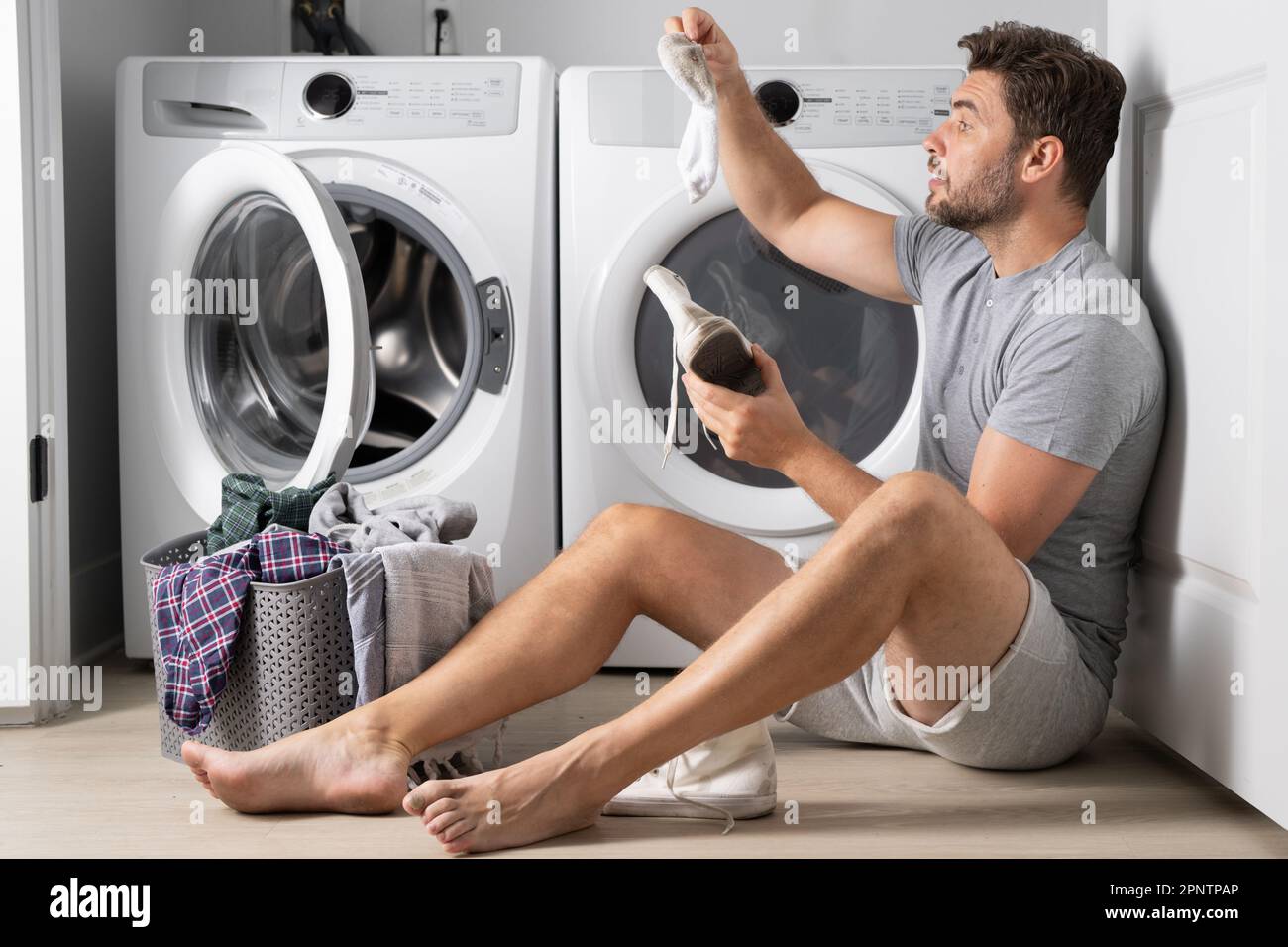 Homme avec des vêtements près de la machine à laver. Beau homme assis  devant le lave-linge. Charge le lave-linge avec du linge sale. Homme  nettoyant des vêtements. Travaux ménagers Photo Stock -