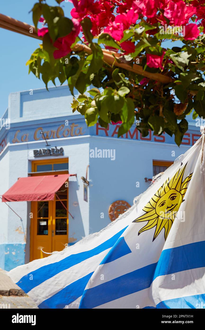 Le drapeau de l'Uruguay avec la façade extérieure d'un magasin d'architecture coloniale en arrière-plan, Colonia del Sacramento, Uruguay. Banque D'Images