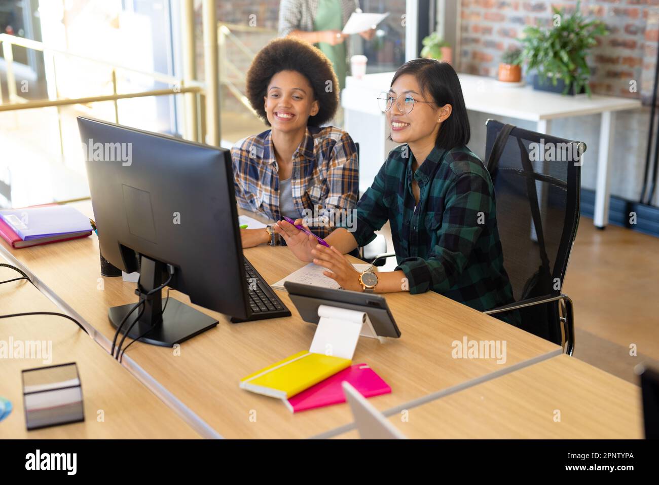 Deux femmes créatives joyeuses et variées sur ordinateur, faisant des appels vidéo dans un bureau décontracté Banque D'Images