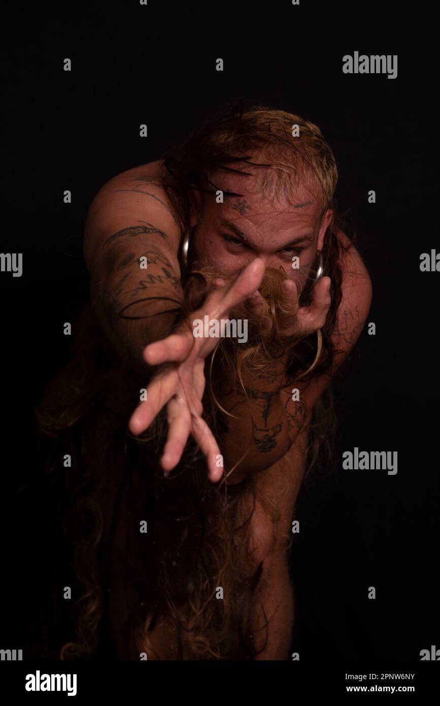 Jeune homme, acteur, portant bikini dans performance gorilla femme avec les cheveux partout dans son corps et expression de la douleur. isolé sur fond sombre. Banque D'Images