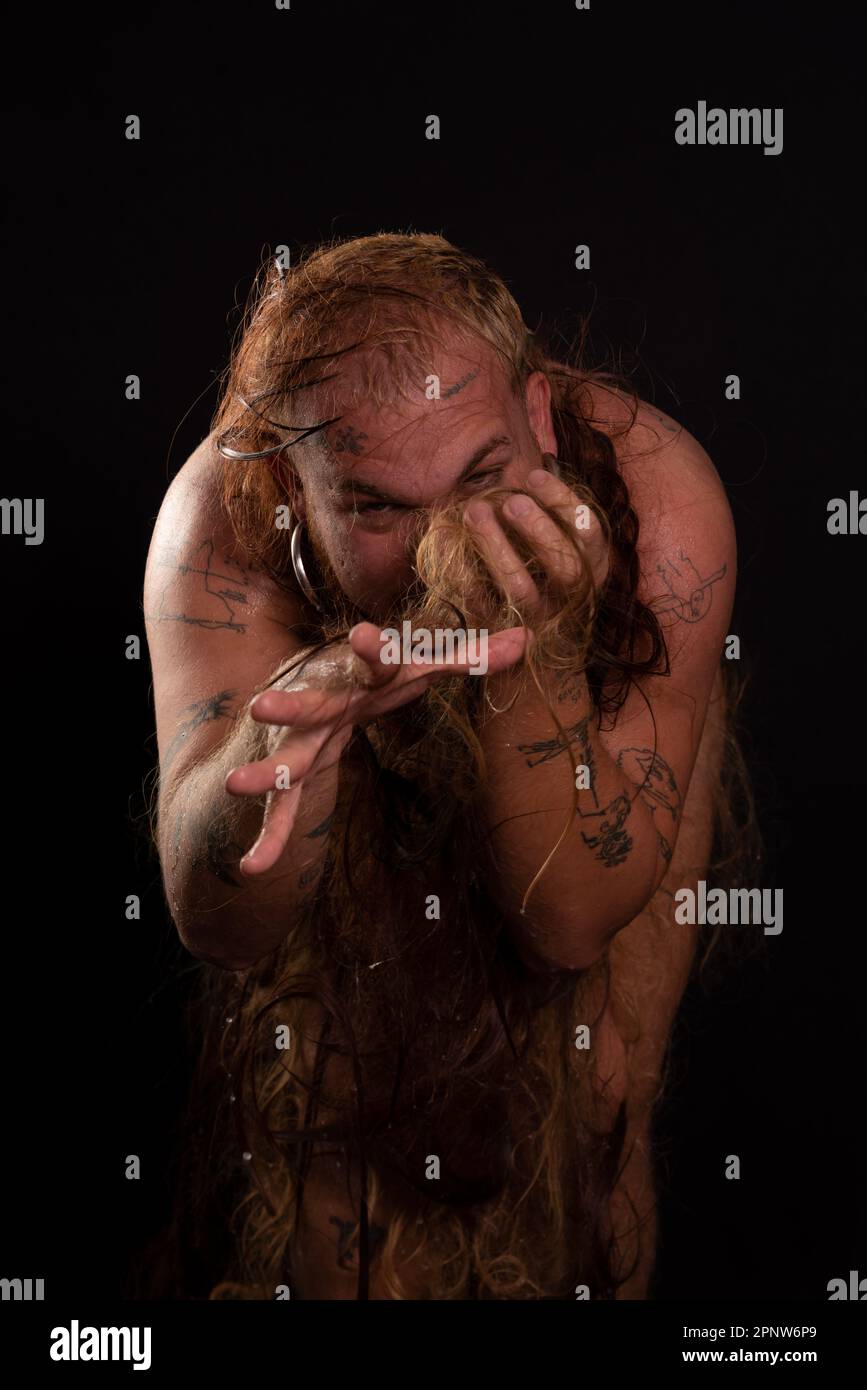 Jeune homme, acteur, portant bikini dans performance gorilla femme avec les cheveux partout dans son corps et expression de la douleur. isolé sur fond sombre. Banque D'Images