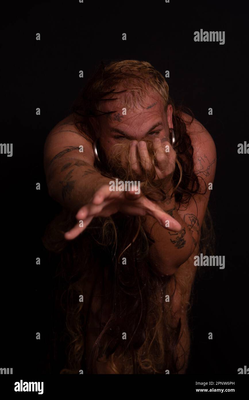 Jeune homme, acteur, portant bikini dans performance gorilla femme avec les cheveux partout dans son corps et expression de la douleur. isolé sur fond sombre. Banque D'Images