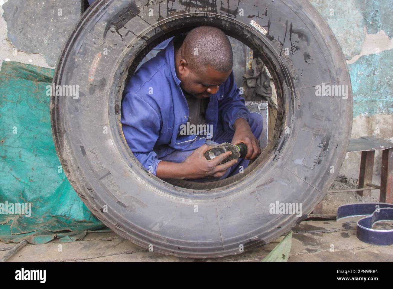 Luke Mwamba se met en train à Kanyama, Lusaka, Zambie, sur 18 janvier 2022. Mwamba, qui a réparé les pneus depuis 2015, dit que la saison des pluies apporte plus d'affaires en raison de mauvaises conditions routières. (Prudence Phiri/Global Press Journal) Banque D'Images