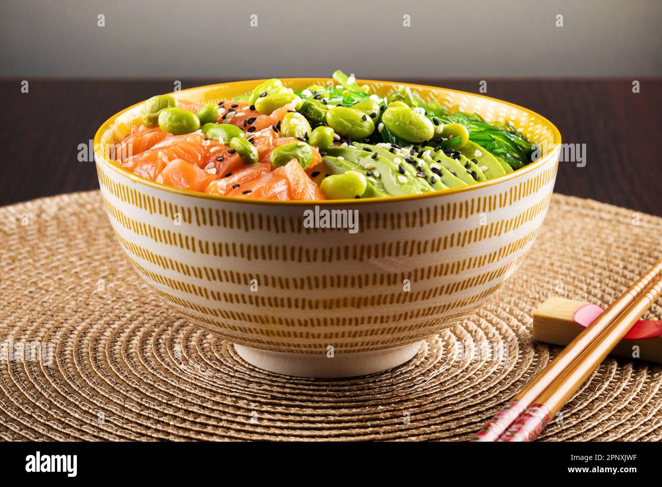 Un appétissant bol de poke sain avec du saumon et des légumes servis avec des graines de sésame et des baguettes sur la table Banque D'Images