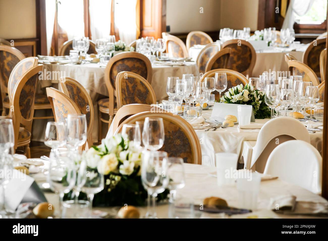 Tables servies avec verres à vin et assiettes blanches avec couverts et serviettes préparées pour la célébration de mariage dans un restaurant léger Banque D'Images