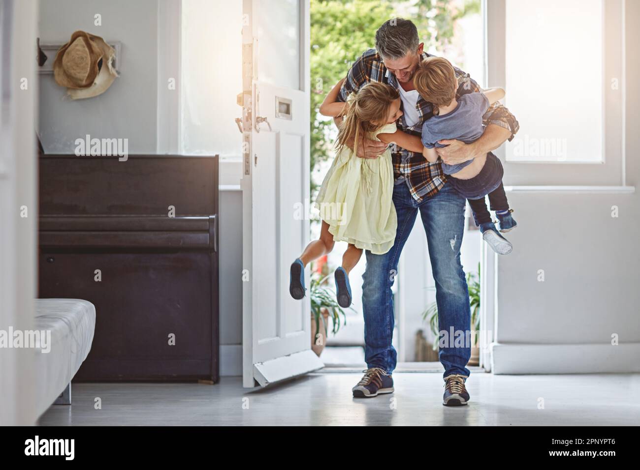 Je t'ai tellement manqué les gars. un père embrassant ses deux enfants lorsqu'il entre dans la maison. Banque D'Images