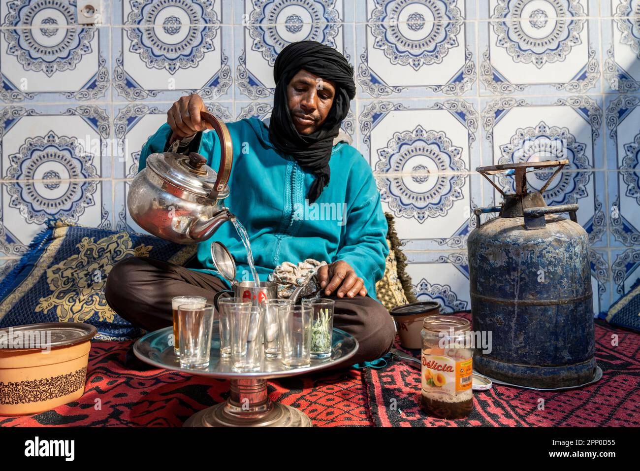 Berbère vêtu de djellaba et de turban noir servant du thé de façon traditionnelle. Banque D'Images